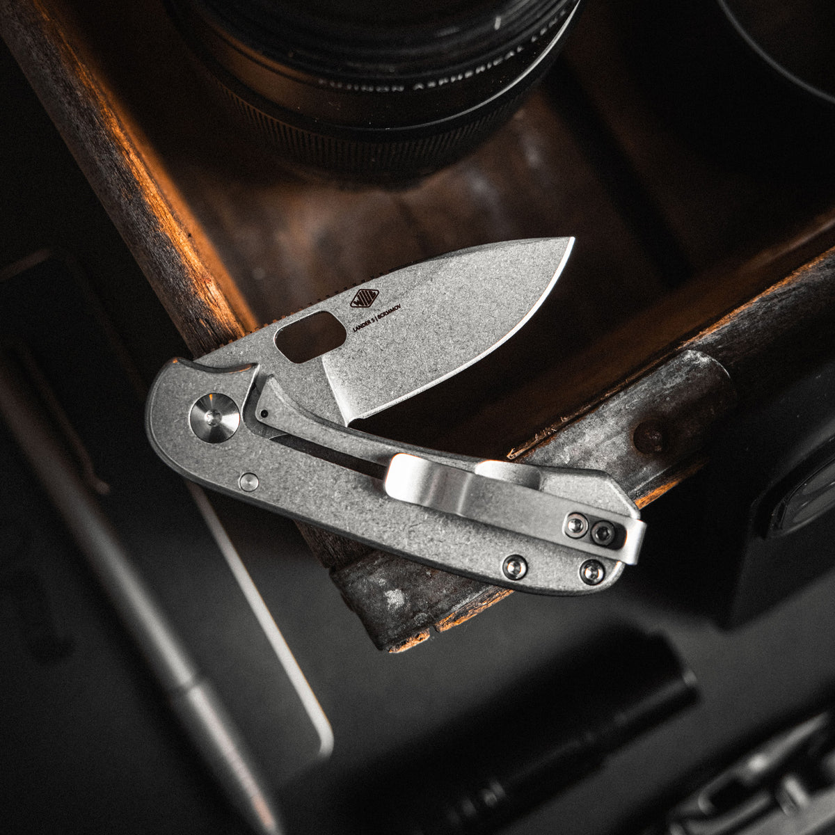 Folding knife on a wooden surface with a camera lens in the background