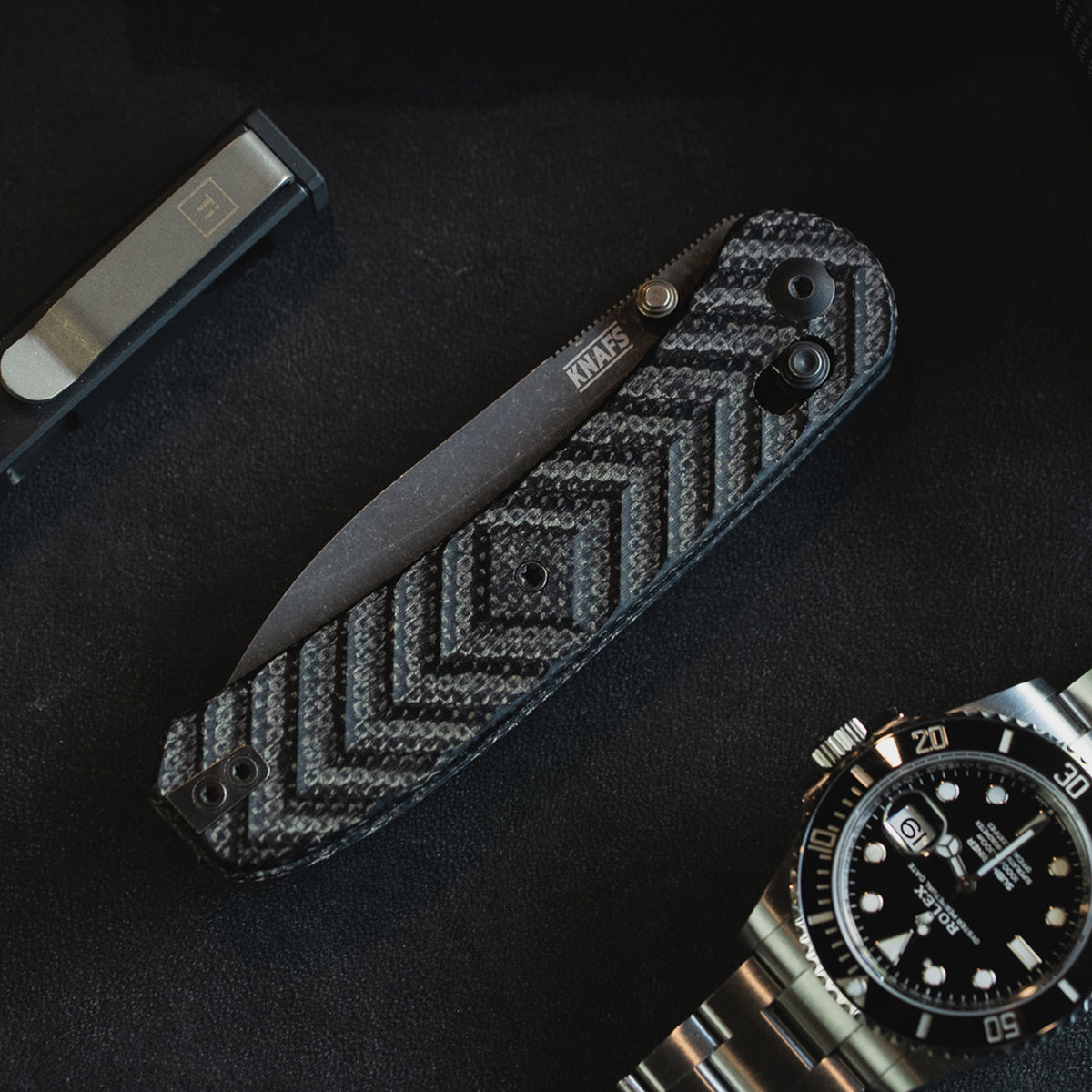 Jeremy Siers Lander 2 knife with black micarta handle next to wristwatch on dark background