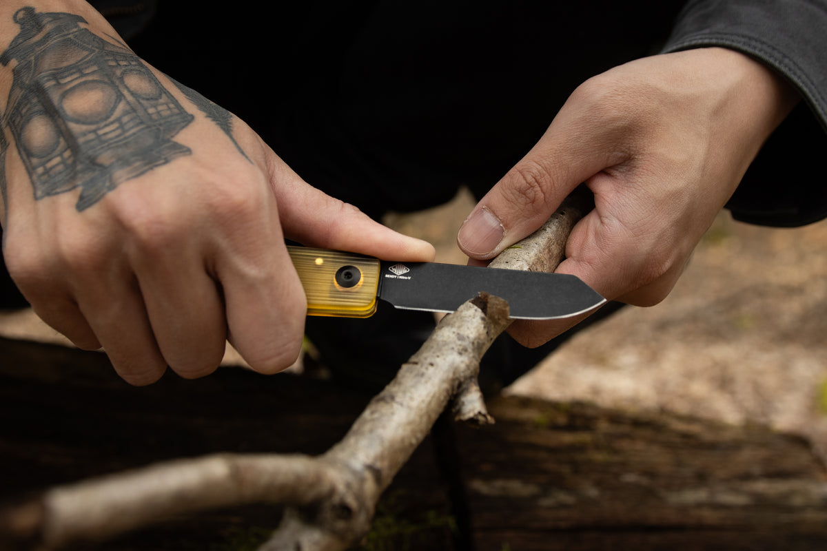 Hands feathersticking a tree branch with open Slippy Sendy pocket knife, tan Ultem handle