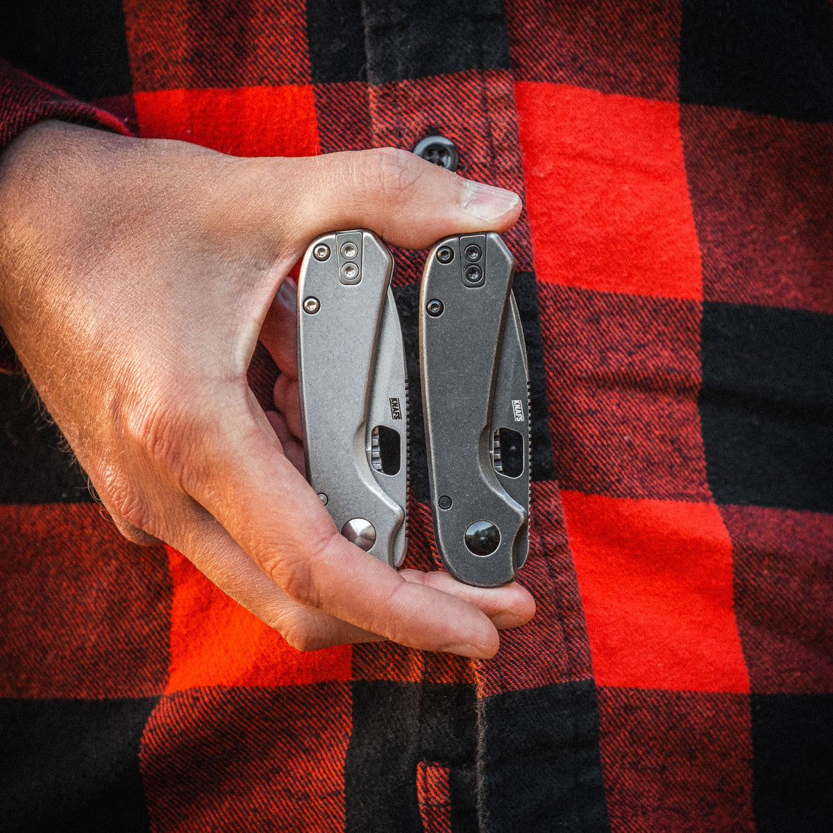 Hand holding two Lander 5 folding knives against a red and black checkered background