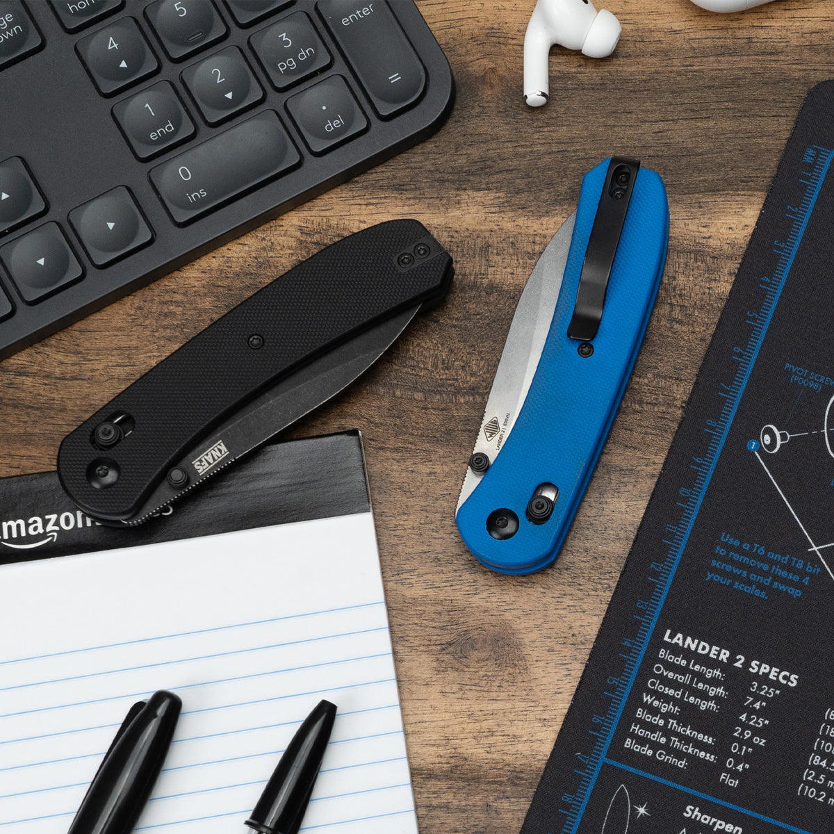 Lander 2 Pocket Knife in Black G10 on a desk with pens and a notebook