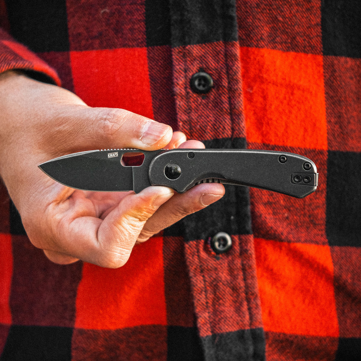 Hand holding Lander 5 folding knife against a red and black plaid shirt background