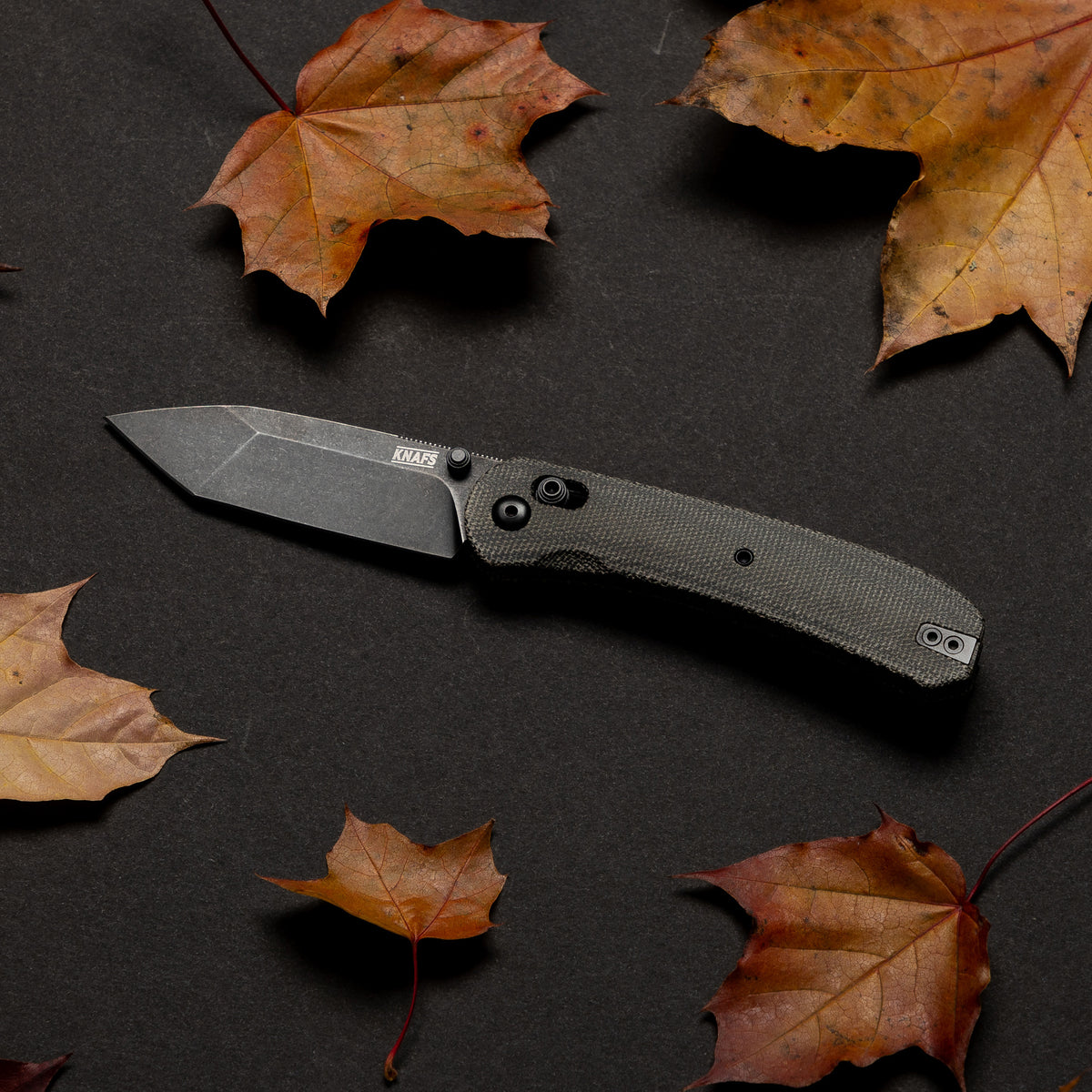 Lander 2 pocket knife with charcoal micarta handle, closed, on black background with autumn leaves