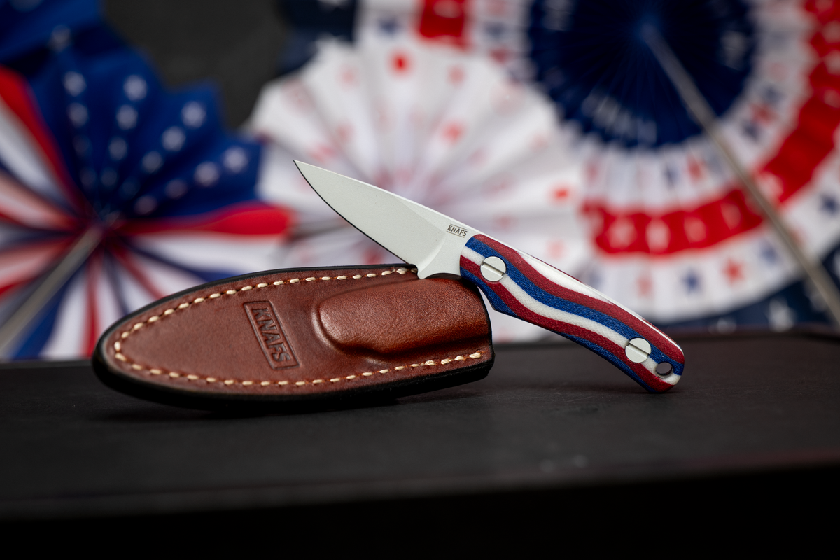 Little Lulu fixed blade knife with red white and blue Americana handle in leather sheath, close-up on patriotic fabric background