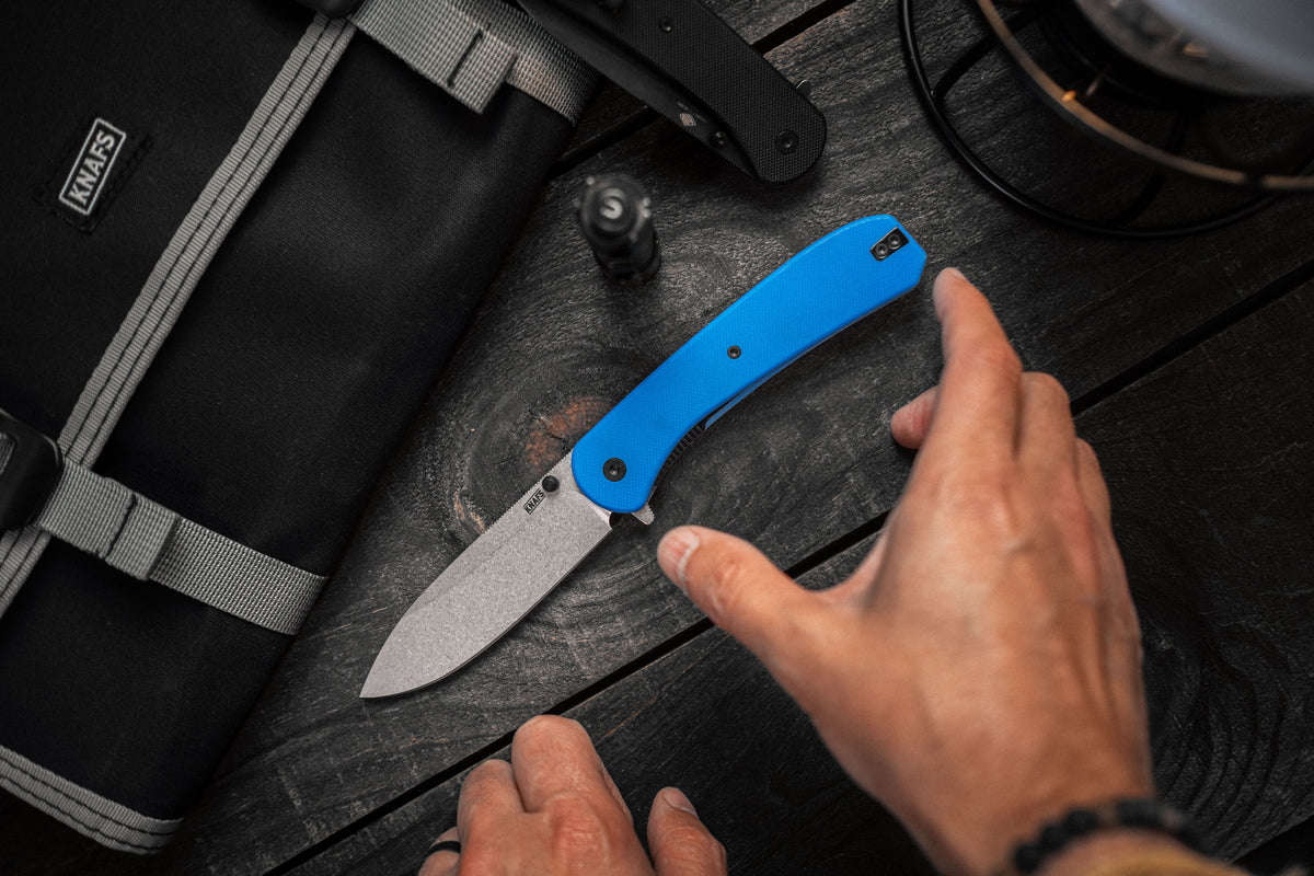 Lander 7 pocket knife with blue G10 handle clipped to backpack strap outdoors