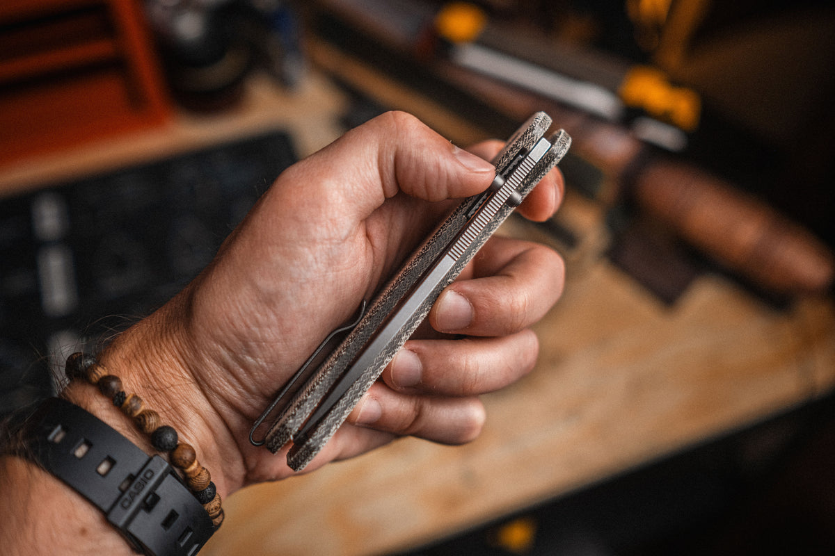 Hand holding Lander 7 pocket knife with Moondust micarta handle at workbench