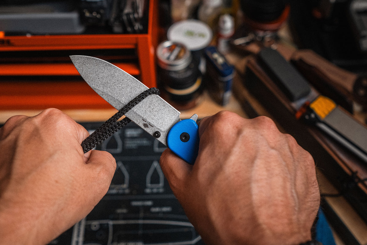 Hands holding Lander 7 pocket knife with blue G10 handle near watch and gear on tailgate