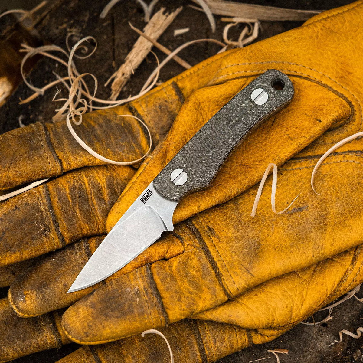 Little Lulu stonewashed fixed blade knife resting on leather next to a campfire