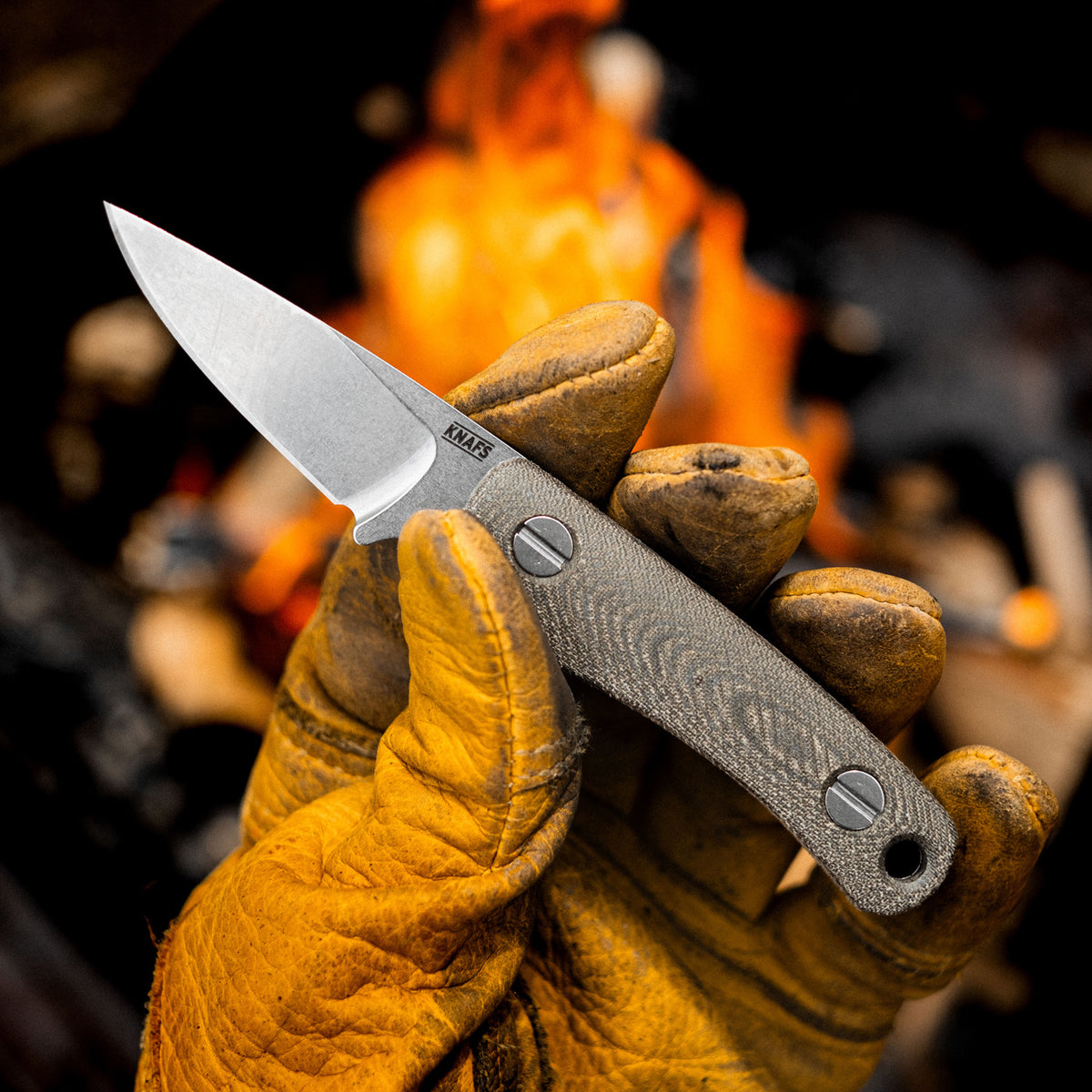 Little Lulu stonewashed fixed blade knife held near a campfire by a leather-gloved hand