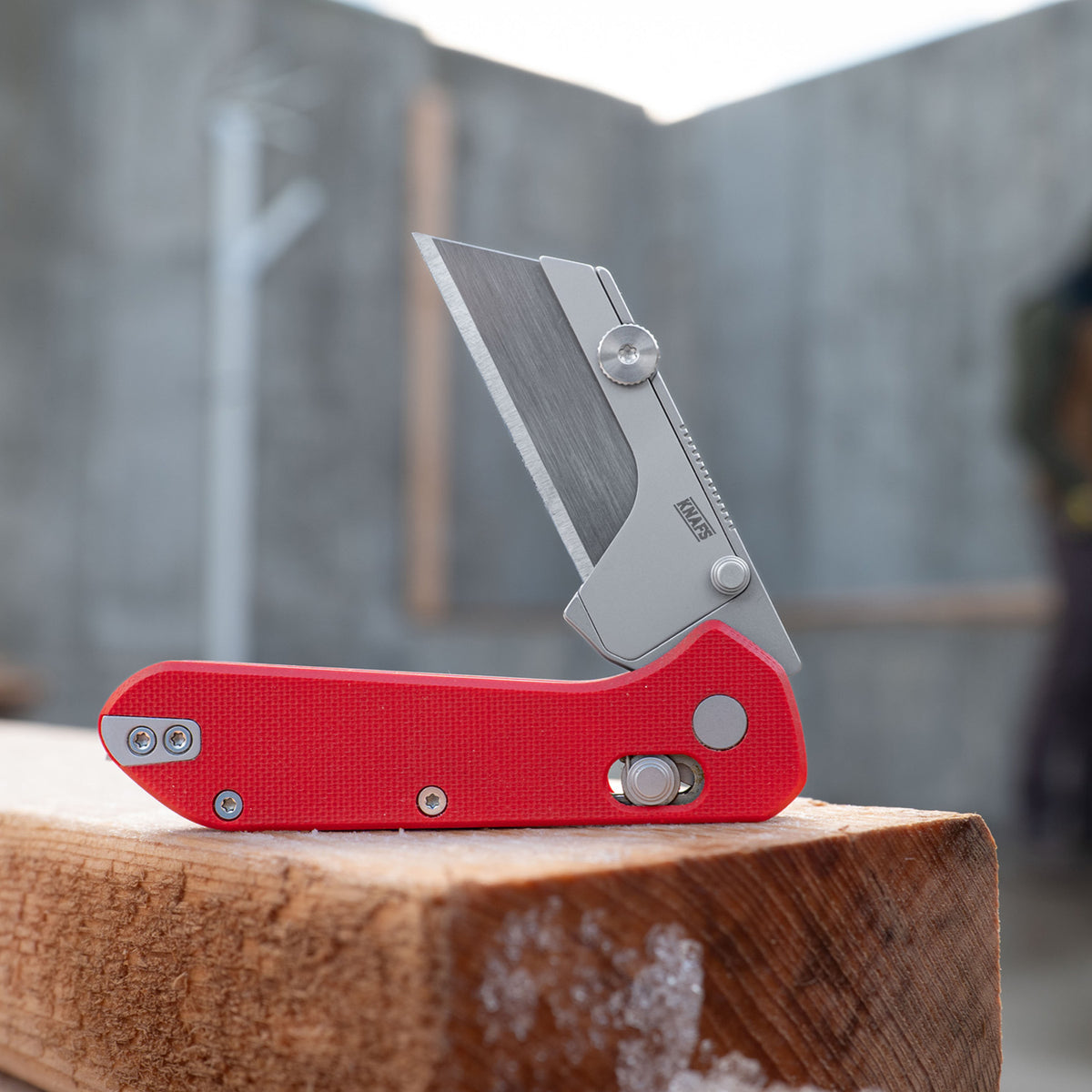 Yuti utility knife with red G10 handle, closed, resting on wood surface
