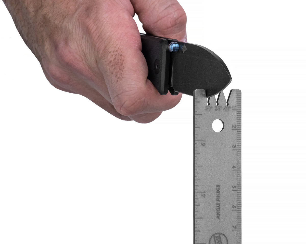 Close-up of a hand using the Titanium Ruler's angle finder cutout to check a folding knife's blade edge angle