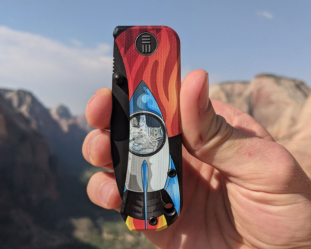 Mars Kitty Banter Scales Version 2.0 knife held in hand with red rock canyon scenery in the background