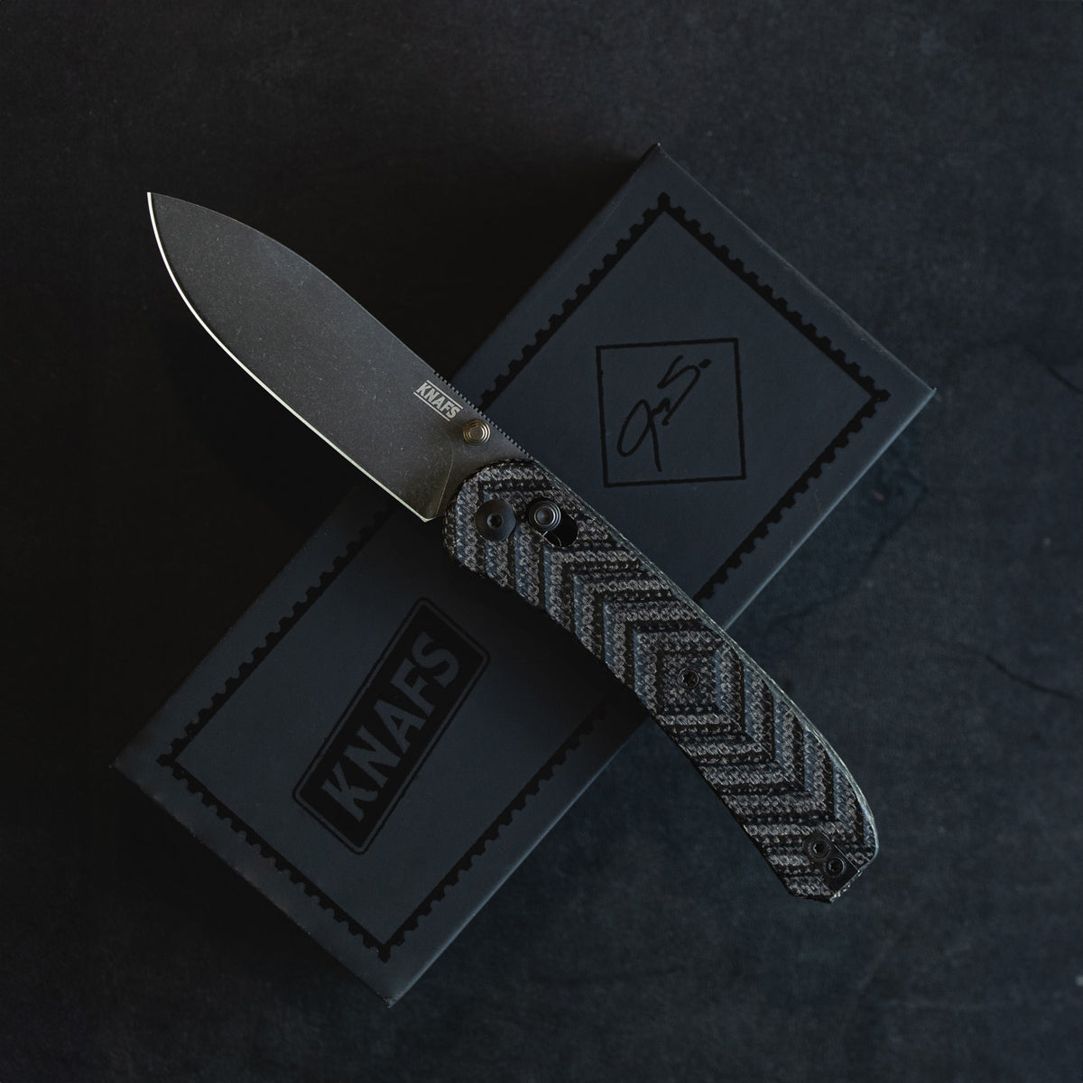 Jeremy Siers Lander 2 knife with black micarta handle, closed, resting on wood surface