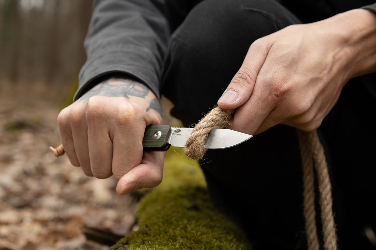 Hand slicing rope outdoors with open Slippy Sendy pocket knife