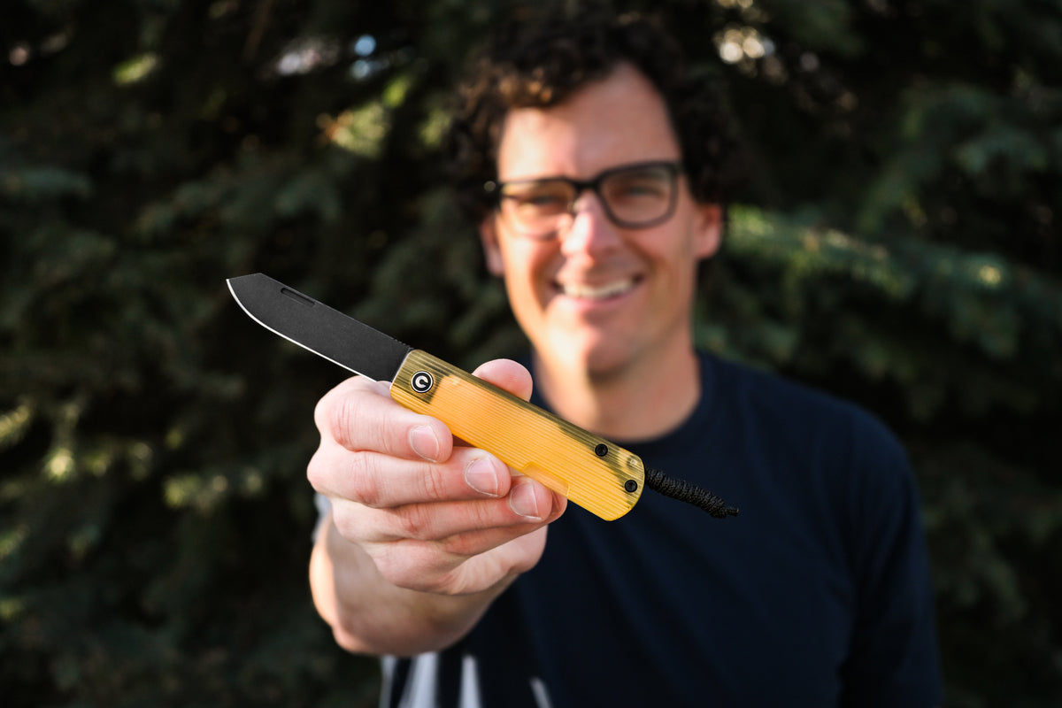 Smiling man wearing glasses holding open Slippy Sendy pocket knife with tan handle