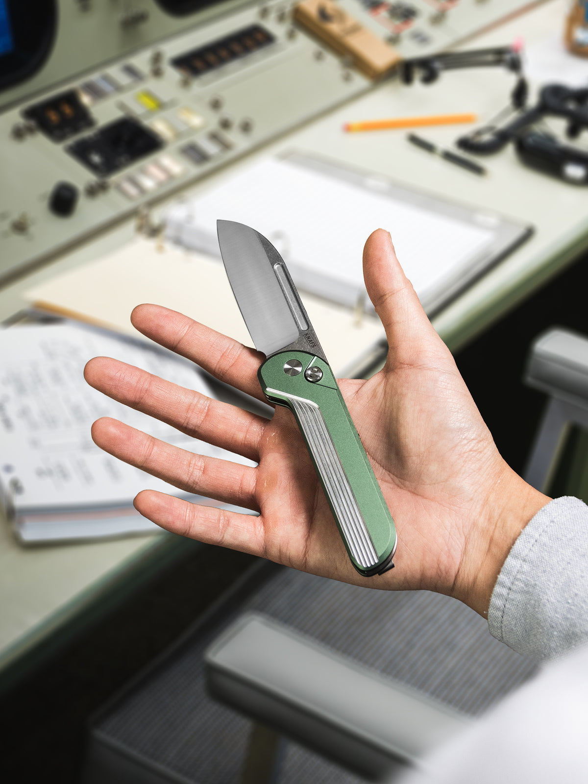 Hand holding open Capcom pocket knife with Mission Control green handle
