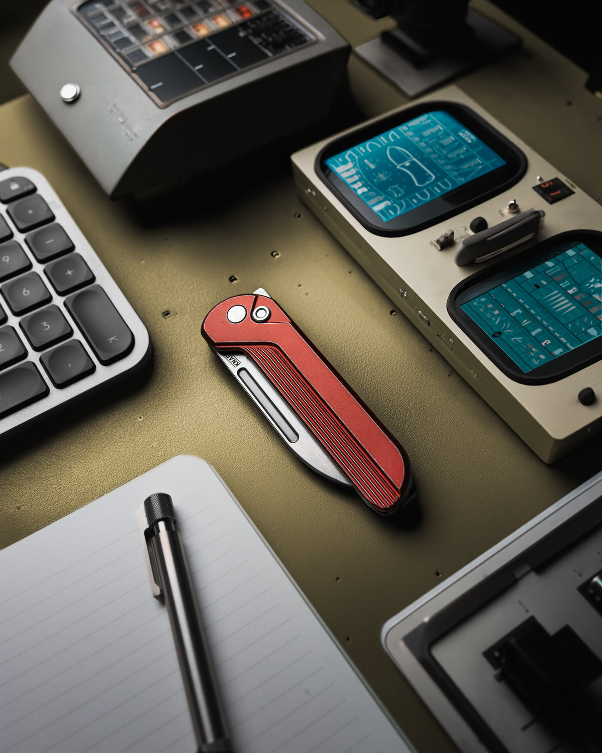 Capcom pocket knife with Re-Entry Red handle, closed, on desk with keyboard and pen
