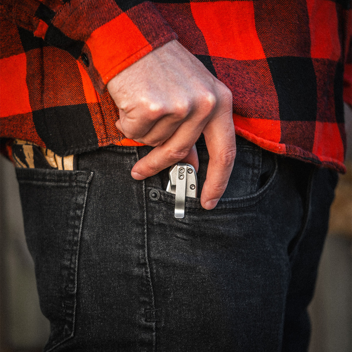 Person wearing a red and black plaid shirt with a pocket knife in jeans.