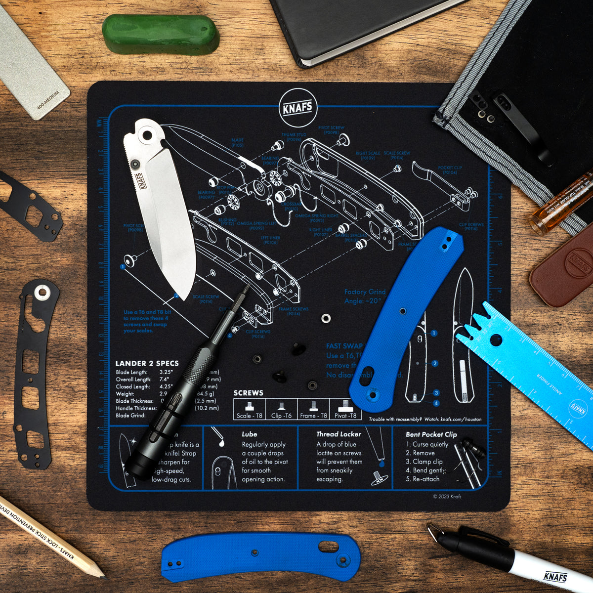 Shop Mat mouse pad for Lander 2 printed with knife diagrams, shown in a workshop with the knife and tools