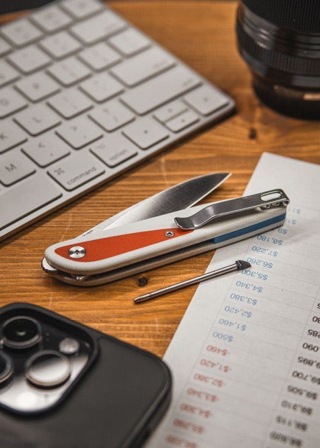 Doodler pocket knife with white and red handle on desk beside keyboard and other EDC gear