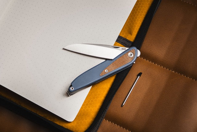 Doodler pocket knife with horizon blue handle and pen tip resting on notebook and desk