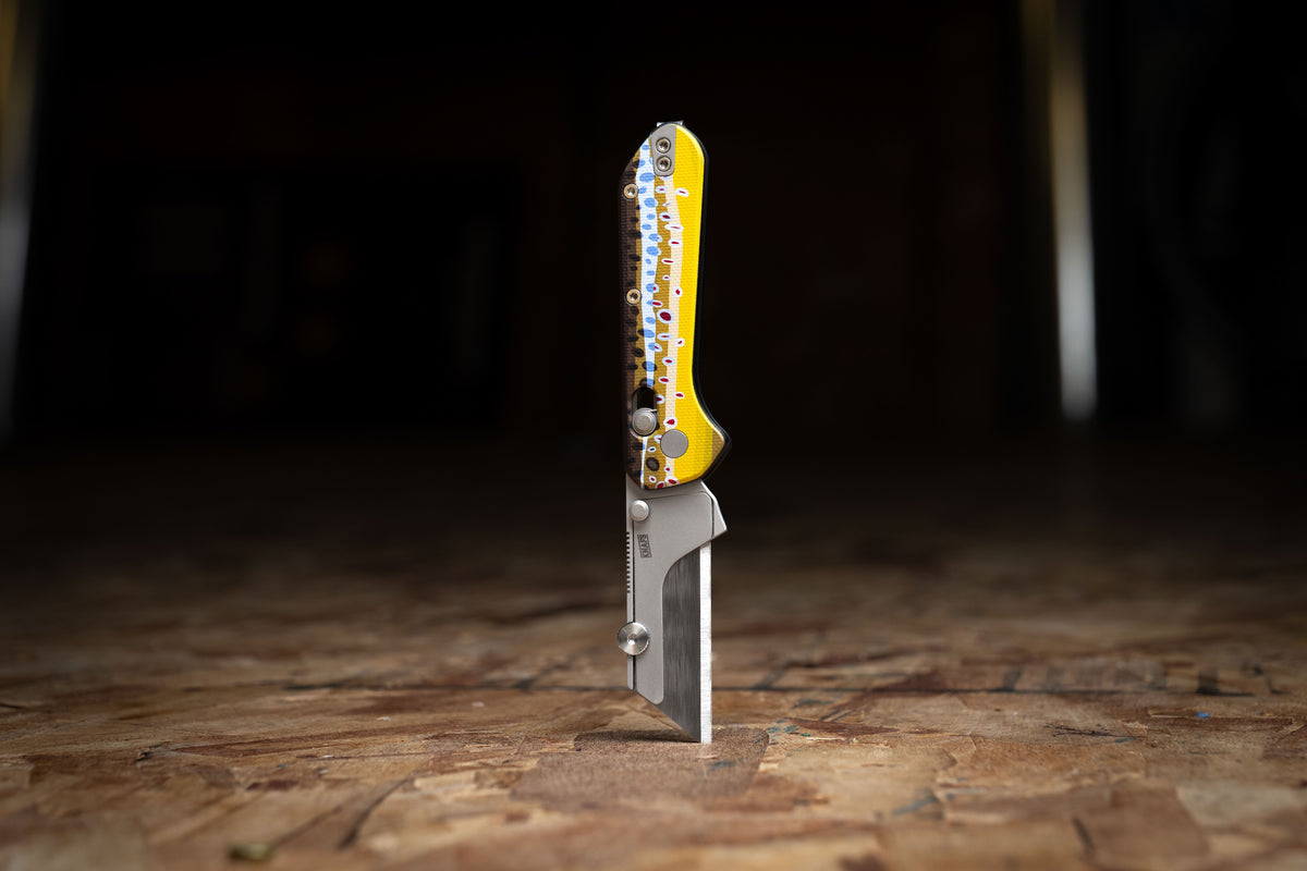 Yuti utility knife with brown trout pattern handle standing upright in dim setting