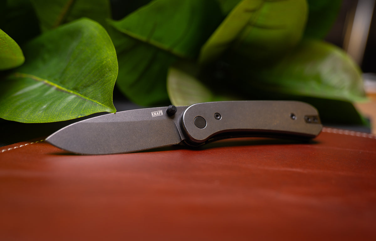 Lander 1 pocket knife with black steel D2 blade, open, resting on green leaves