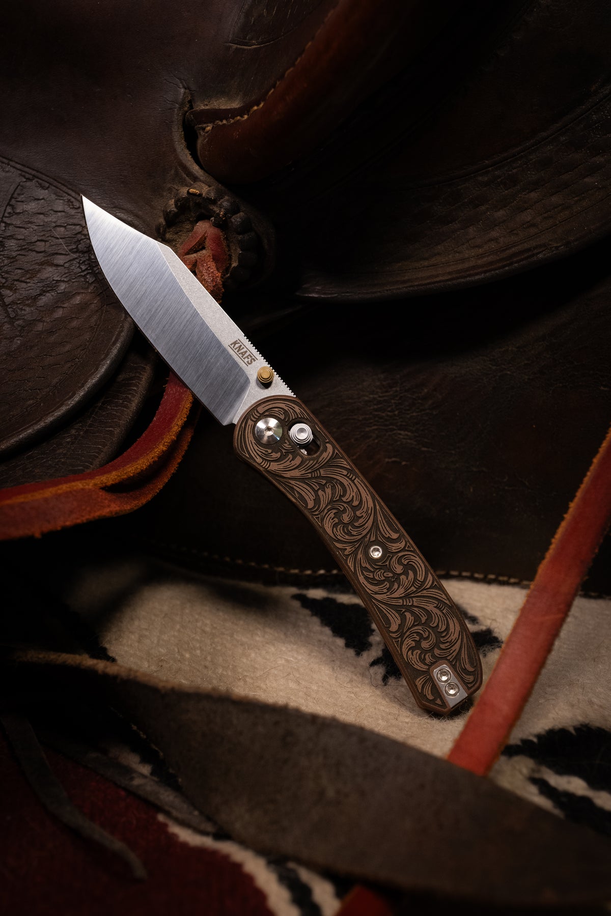Lander 2 knife, Filigree Western clip point edition, closed, resting on leather saddle