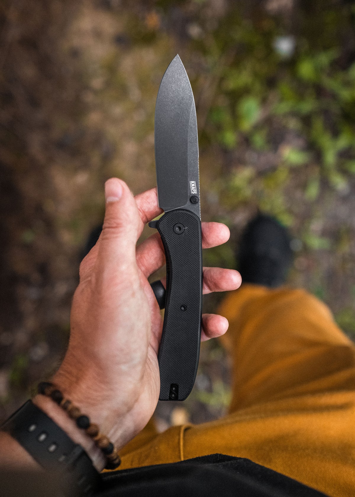 Hand holding open Lander 7 pocket knife with black G10 handle outdoors