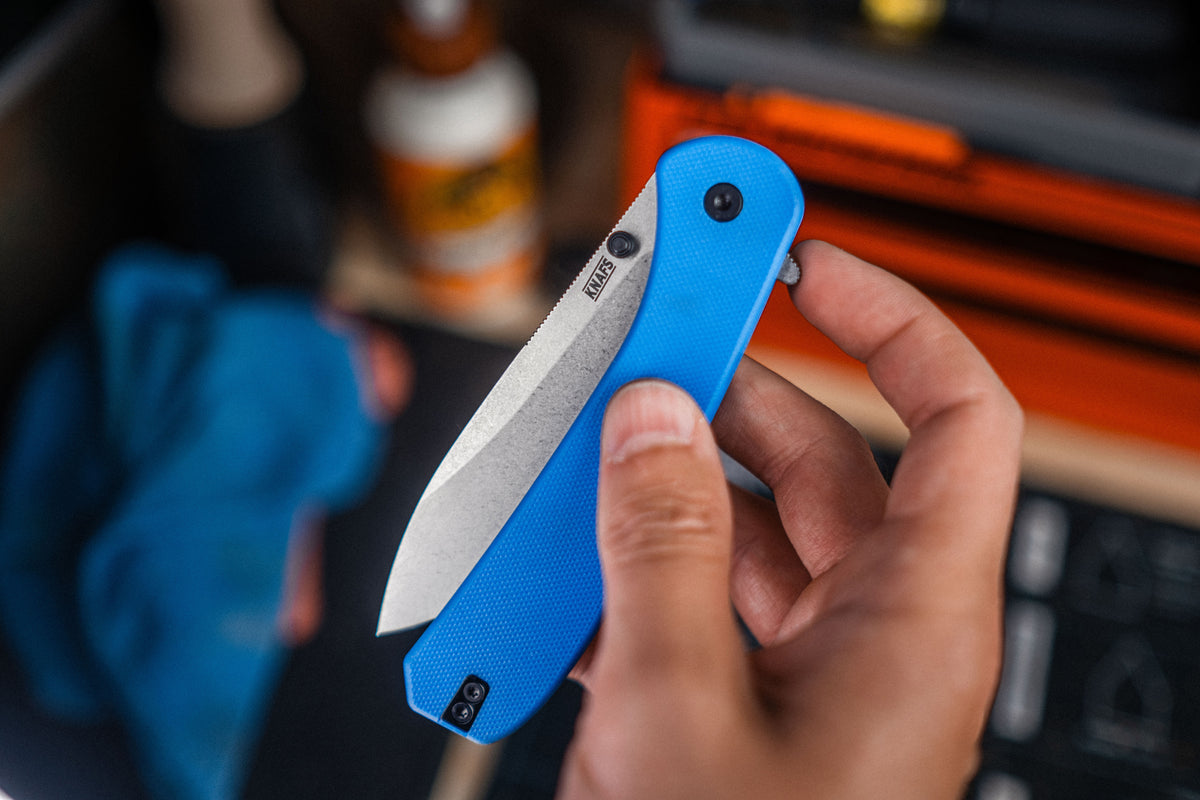Hands opening Lander 7 pocket knife with blue G10 handle outdoors