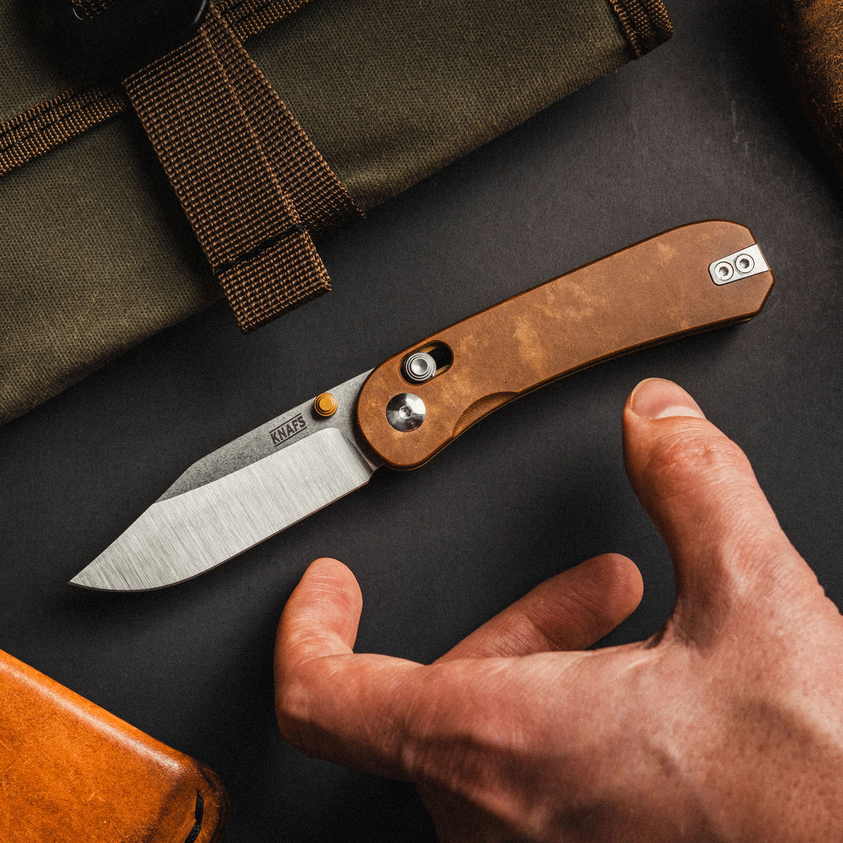 Lander 3 pocket knife with tan handle held in hand on wooden workbench