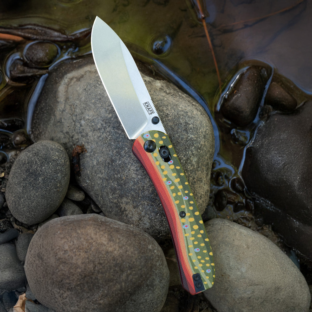 Lander 2 Pocket Knife with printed G10 scales in a Rainbow Trout pattern, open, outdoors on rocks