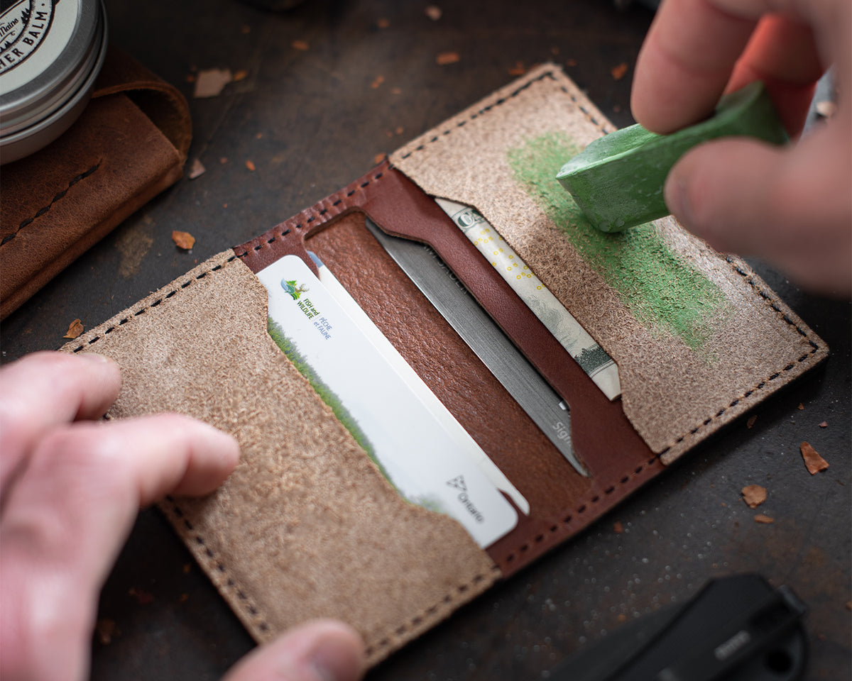 Hands applying green polishing compound to the leather strop inside the wallet