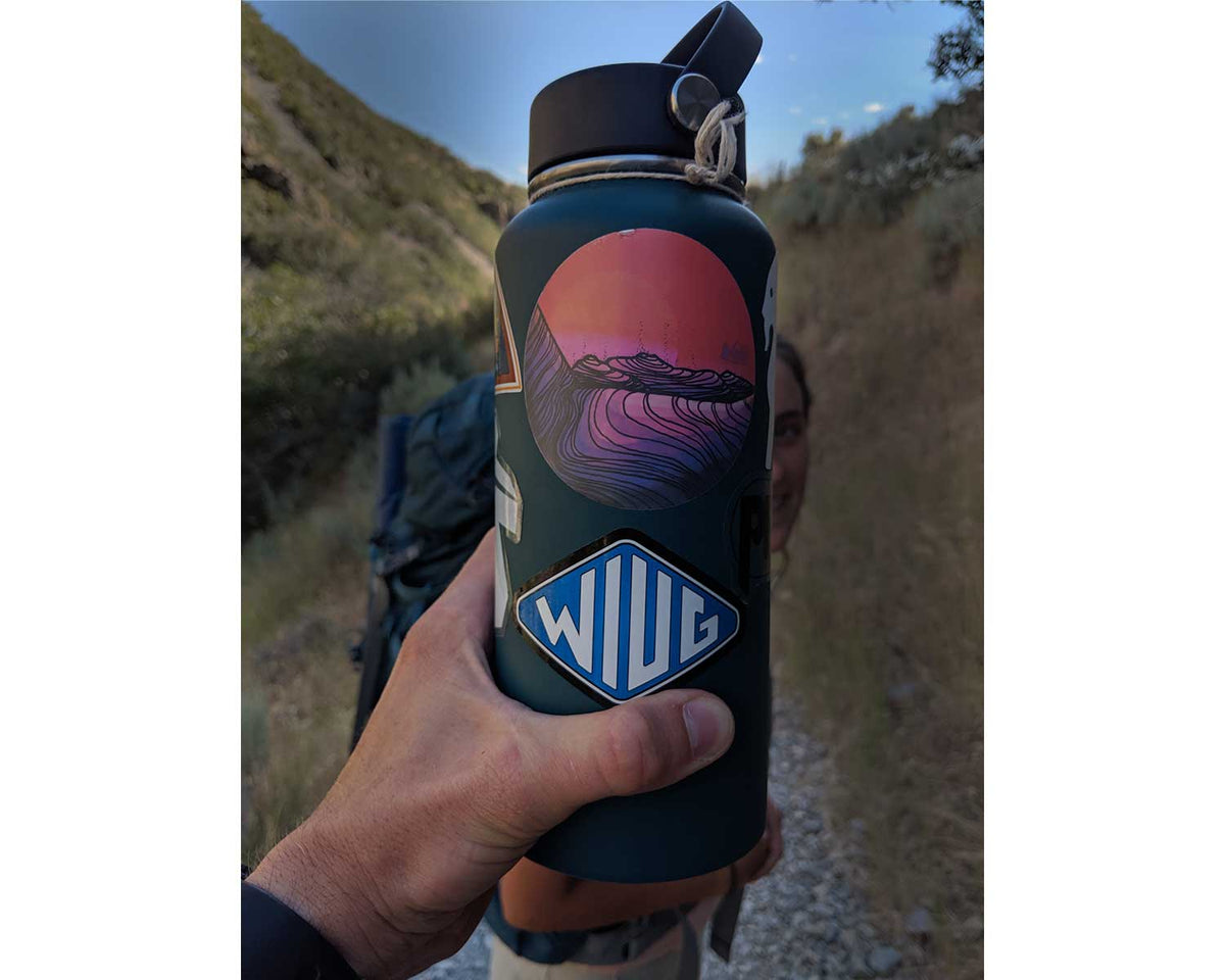 Knafs WIUG sticker applied to a purple water bottle held outdoors on a hike